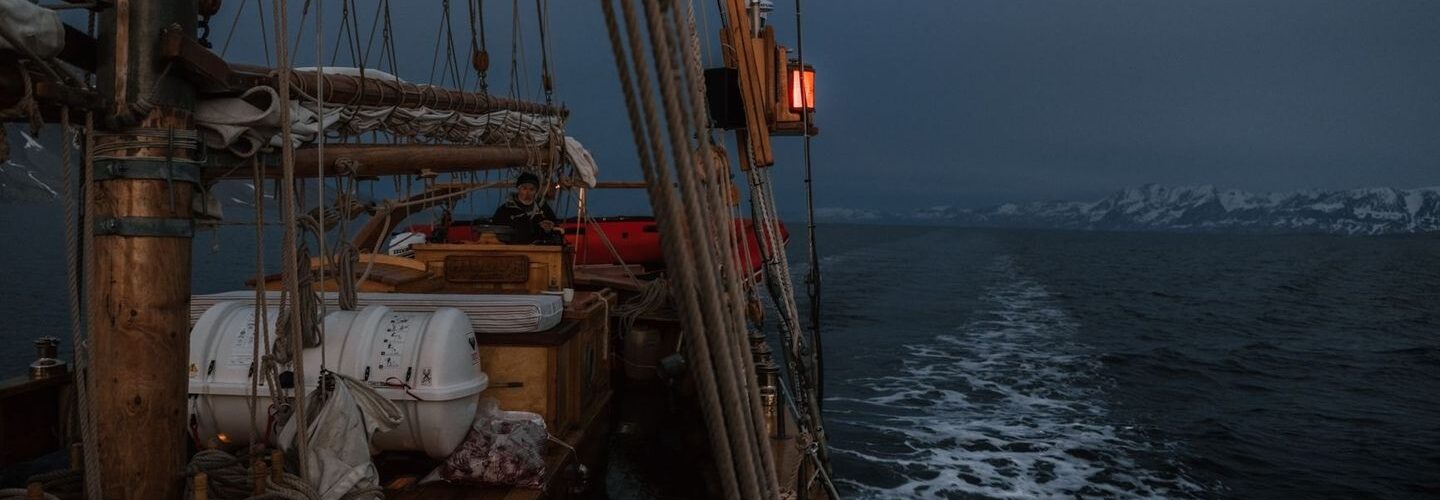 Segelbåt i mörker med rött ljus och snötäckta berg i bakgrunden