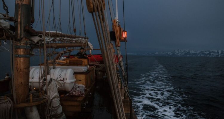 Segelbåt i mörker med rött ljus och snötäckta berg i bakgrunden